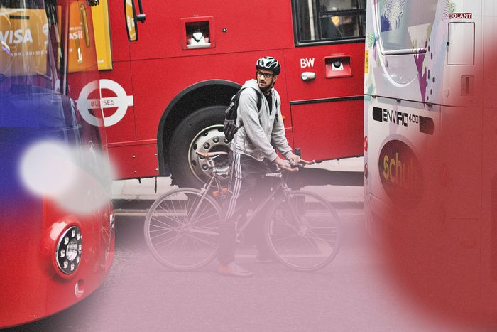 A man in a gray sweatshirt and black sweatpants rides a bicycle between three buses